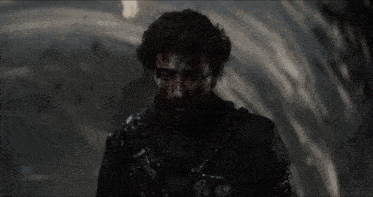 a man with blood on his face is standing in the dark looking at the camera .