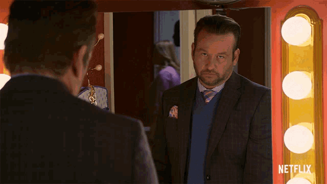 a man in a suit and tie is looking at himself in a mirror with a netflix logo in the corner