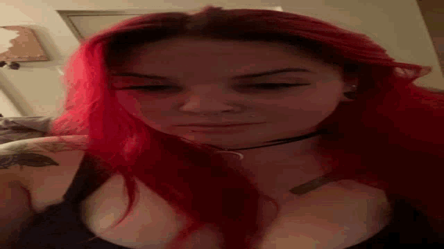 a woman with red hair and a tattoo on her arm is wearing a choker necklace .