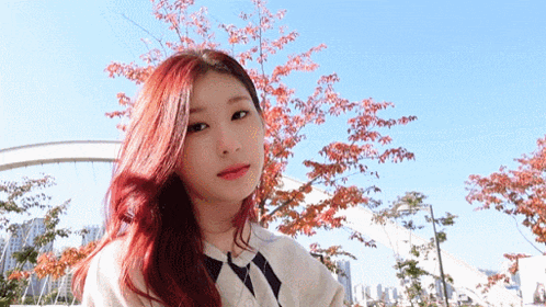a woman with red hair is standing in front of a tree in a park .
