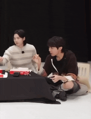 a man is sitting on the floor eating a hamburger while another man sits at a table .