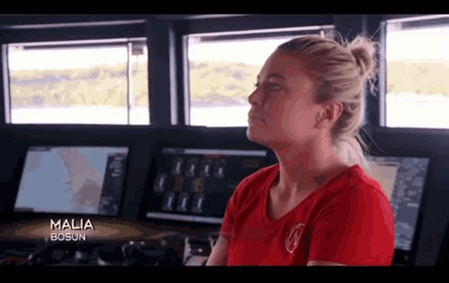 a woman in a red shirt is sitting at a desk in front of a computer monitor on a boat .