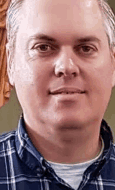 a close up of a man 's face wearing a plaid shirt and smiling .