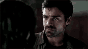a man with a beard is looking at another man in a dark room