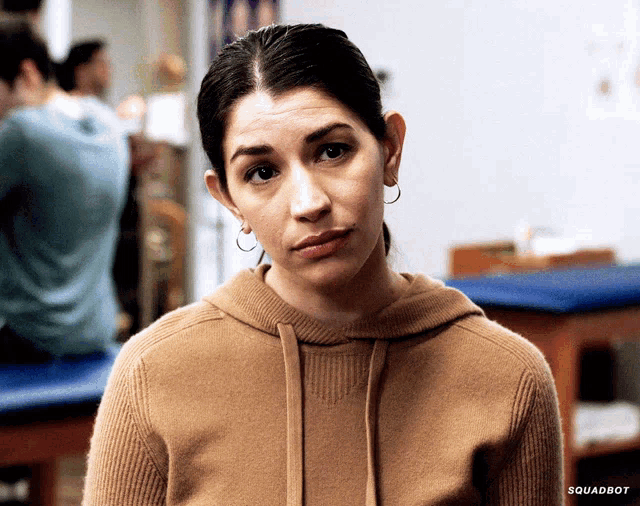 a woman wearing a brown sweater and hoop earrings looks at the camera