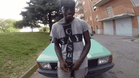 a young man standing in front of a green car wearing a shirt that says " say "