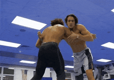 two men are wrestling in a gym with blue ceilings .