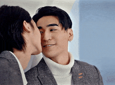 a man kissing another man on the cheek in front of a mirror