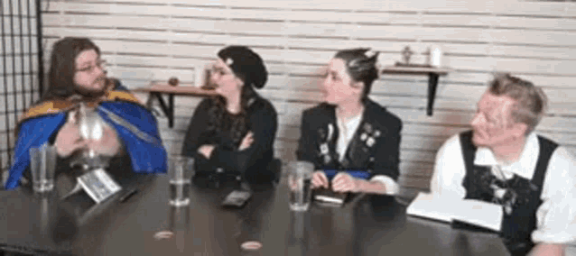 a group of people are sitting at a table with glasses of water and a book .