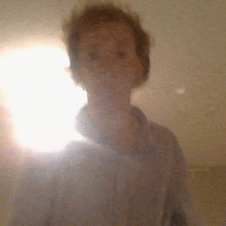 a blurred image of a person taking a selfie with a light behind them
