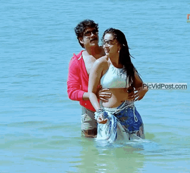 a man and a woman are standing in the water and the website picvidpost.com is visible in the corner