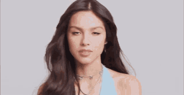 a close up of a woman 's face wearing a necklace and a blue dress .