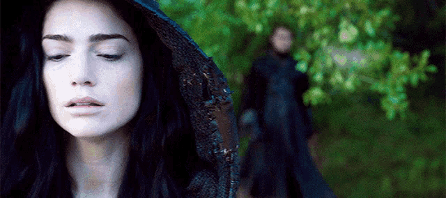 a woman wearing a black hooded cape is standing in front of a man in a black dress .
