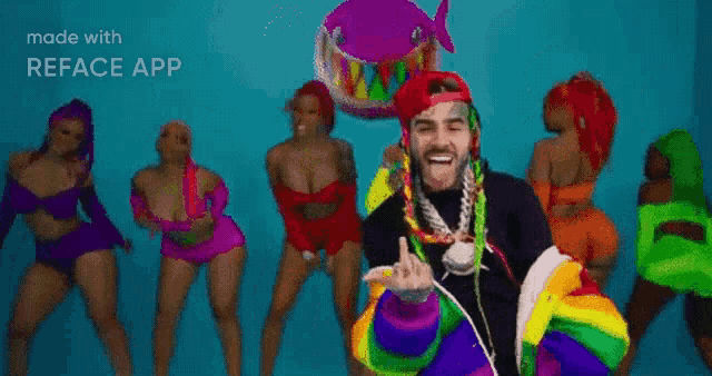 a man wearing a rainbow hat and necklace is standing in front of a group of women dancing .