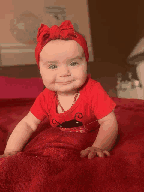 a baby wearing a red shirt and a red headband smiles for the camera