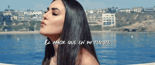 a woman with long hair stands in front of a body of water with el amor que en mi tuviste written below her
