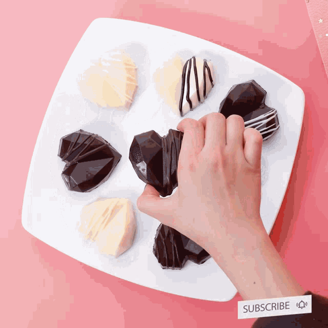 a person holding a heart shaped chocolate on a white plate with a subscribe tag