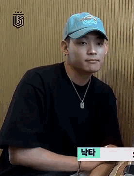a young man wearing a black shirt and a blue hat is sitting down .