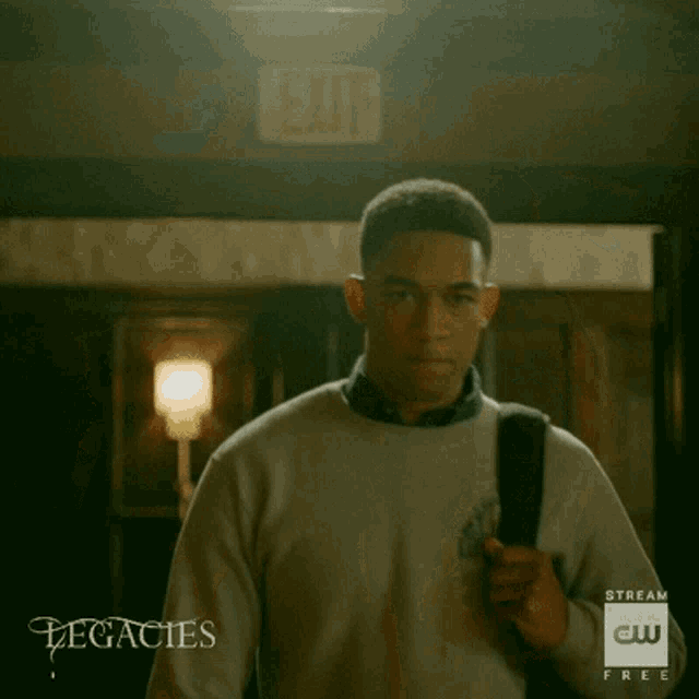 a young man wearing a white sweater and a backpack is standing in a room .