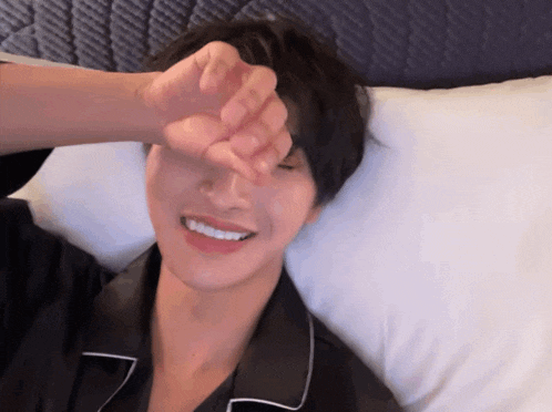 a young man laying on a bed with his hand on his face