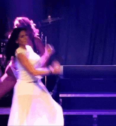 a woman in a white dress is dancing in front of a microphone on a stage