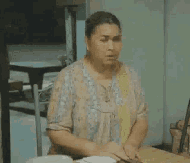 a woman is sitting at a table with a plate of food in front of her and making a funny face .