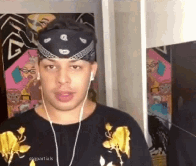 a man wearing a bandana and headphones is standing in front of a painting .