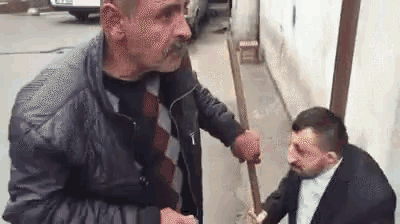 two men are standing next to each other on a sidewalk . one of the men is holding a stick in his hand .