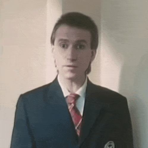 a man in a suit and tie is standing in front of a white wall .