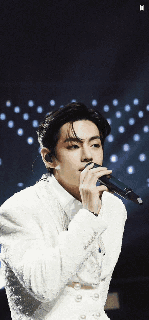 a man in a white jacket is singing into a microphone on a stage