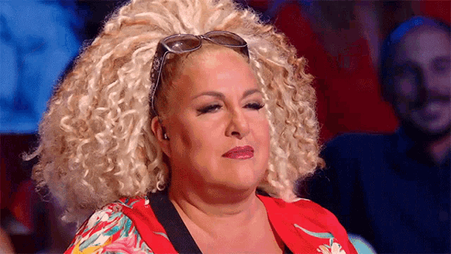 a woman with blonde curly hair is wearing sunglasses and a red top .