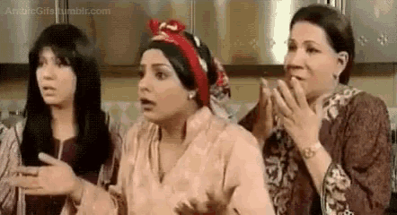 three women are standing in a kitchen with their hands in the air .
