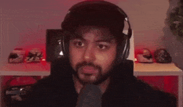 a man with a beard wearing headphones is sitting in front of a table with helmets on it .