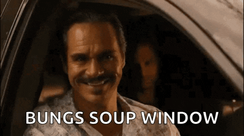 a man with a mustache is sitting in a car with the words bungs soup window written on the screen behind him .