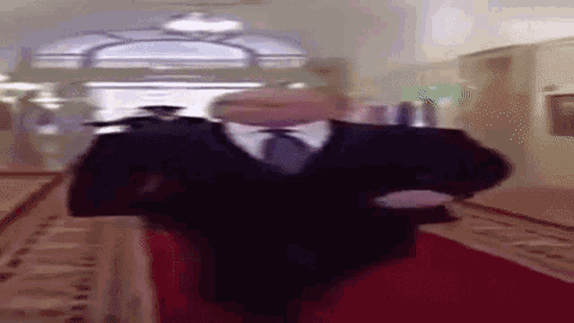 a man in a suit and tie is walking down a red carpeted hallway .