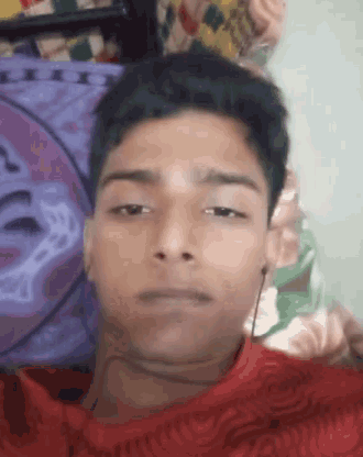 a young man in a red shirt is laying on a bed looking at the camera