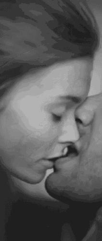 a black and white photo of a man and woman kissing each other .
