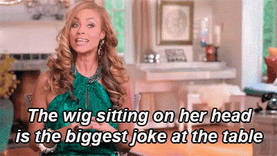 a woman in a green dress is sitting at a table with a wig on her head