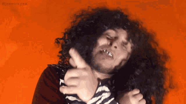 a man with curly hair giving a thumbs up sign