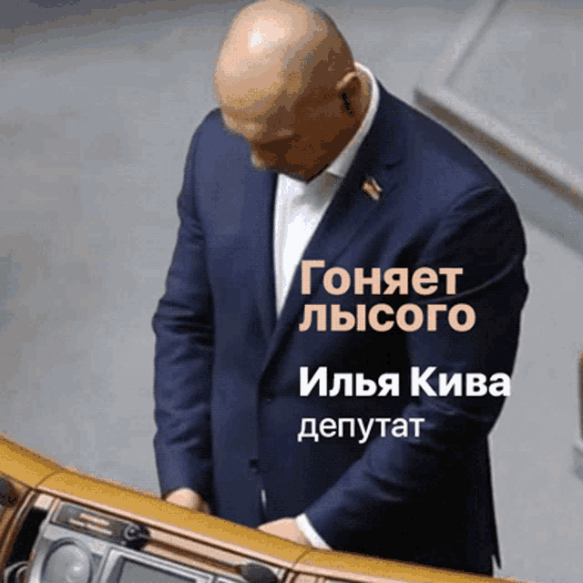 a man in a suit stands in front of a podium with the name ilya kiva written on it
