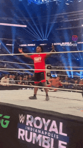 a man in a red shirt stands in a wrestling ring in front of a royal rumble sign