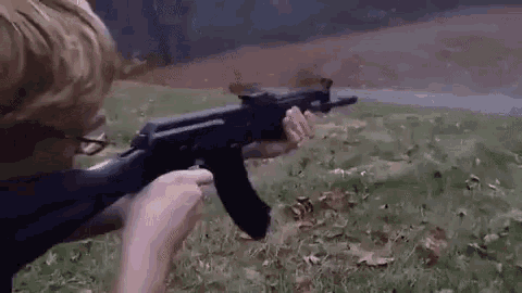 a young boy is holding a gun in his hands and shooting it .