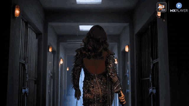 a woman is walking down a hallway with a mxplayer logo on the bottom