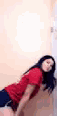 a woman in a red shirt and shorts is leaning against a door .