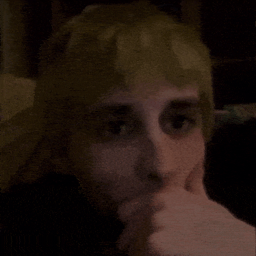 a person with blonde hair is covering their mouth with their hand