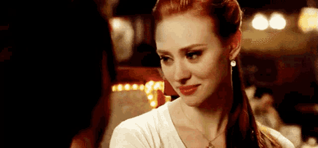 a woman with red hair is wearing a white t-shirt and a necklace .