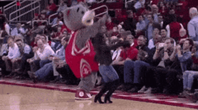 a mascot is dancing on a basketball court with a crowd watching .