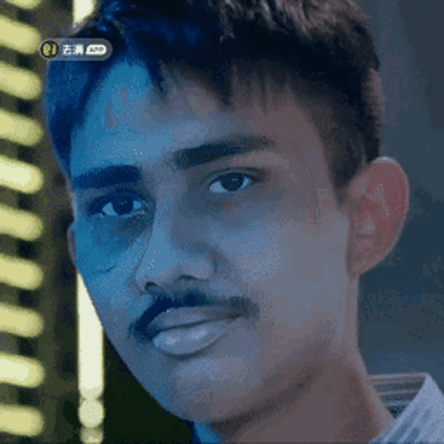 a man with a mustache is looking at the camera with a blue light behind him