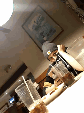 a person wearing a beanie is sitting at a table with a picture on the wall behind them