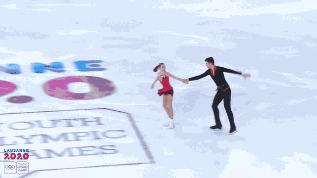 a couple of people are ice skating in front of a lausanne 2020 banner